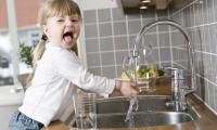 Leitungswasser (Trinkwasser): kleines Mädchen spielt mit dem Trinkwasser aus Wasserhahn in Küche.