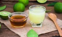 Fresh squeezed lime juice in a glass, with a bowl containing honey to the left and surrounded by limes.