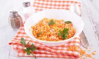 Lentils, red, cooked in white bowl on folded tablecloth.