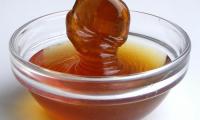 Malt syrup (malt extract) flows into a small transparent glass bowl.