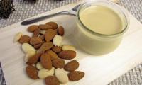 Light, home-made almond puree in glass jar, with almonds next to it.