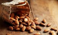 Almonds—Prunus dulcis—spilling out of a small basket onto a wooden table.