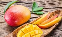 Mango, crudo - Mangifera indica: Tagliato a pezzi (su tavola di legno), davanti a un mango intero.