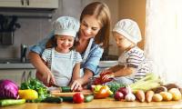 Madre con dos niños pequeños prepara una ensalada de verduras con ellos