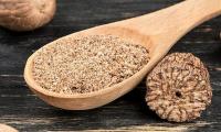 Wooden spoon with grated nutmeg and a partly grated nutmeg next to it.