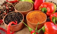 Two shades of ground paprika and paprika seeds in bowls surrounded by different chili varieties.