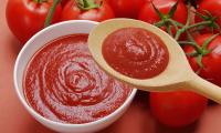Passierte Tomaten in einer Keramikschüssel und auf Holzkelle, darum herum Tomaten.