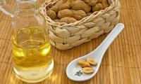 A carafe of peanut oil, peanuts in their shell to the right, and a spoonful of shelled peanuts in the foreground.