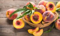 Fresh peaches in and beside a woven basket — some of them are cut open.