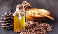 Pine nuts, raw, unpeeled, peeled in bowl behind, next to pine nut oil, pine cones.