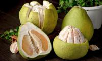 Pomelo (not grapefruit) whole, half peeled and half fruit on dark table.