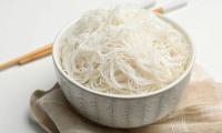 Cooked rice noodles in bowl, behind of that a pair of eating sticks.