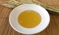 Rice syrup on a white plate. In the background, rice on a brown bamboo mat.