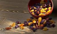 Various types of raisins in brown ceramic bowl, part of the raisins lying in front of it.