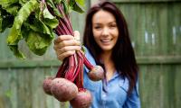 A young gardener is displaying a bundle of fresh red beets—Beta vulgaris.