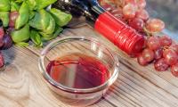 Red wine vinegar in a glass bowl surrounded by grapes and basil.