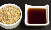 Sesame oil made from roasted sesame seeds (Sesamum indicum) in a bowl, white sesame seeds on left.