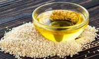 Virgin sesame oil in a glass bowl with white sesame seeds around it