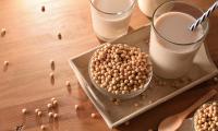 Homemade soy milk in drinking glasses, in front of and next to soybeans open.