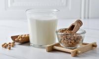 Soy cream with rapeseed oil in a drinking glass, with soybeans left and right next to it.