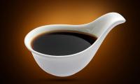 Soy sauce (Tamari) in a small white ceramic chinese spoon against a background in shades of brown.
