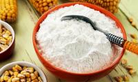 Cornstarch (maize starch) in small orange ceramic bowl surrounded by corn.