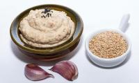 Tahin (sesame butter) in dark brown shell, next to seeds and two garlic cloves.