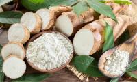 Tapioca starch in a wooden container surrounded by sliced cassava roots.