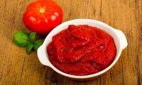 Homemade tomato pulp from Solanum lycopersicum in white ceramic bowl on wooden table.