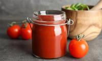 Homemade tomato paste made from fresh tomatoes in a canning jar. Whole tomatoes next to it.