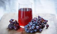 Red grape juice in a glass surrounded by dark grapes.