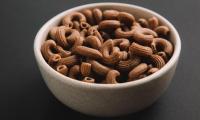 Whole grain elbow macaroni in ceramic bowl on dark background.