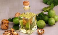 Walnut oil in square glass bottle, surrounded by walnut leaves and nuts with and without outer shell