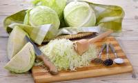 Weisskohl - auf Küchenbrett vorbereitet um Sauerkraut herzustellen, dahinter Weisskohlköpfe.