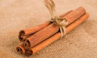 Four cassia cinnamon sticks (1–3 mm thick) tied together on a brown woven fabric.