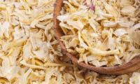 Dried (dehydrated) onions in flake form in wooden vessel and lying next to it.