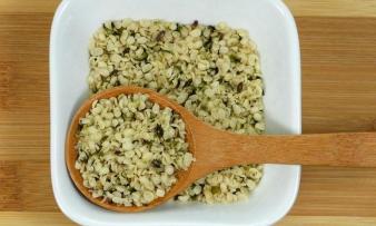 Hanfsamen, geschält, roh - Cannabis sativa - in weisser Porzellanschale mit Holzlöffel.