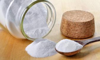 Agente lievitante di soda versato da un contenitore di vetro e un mestolo di legno pieno.